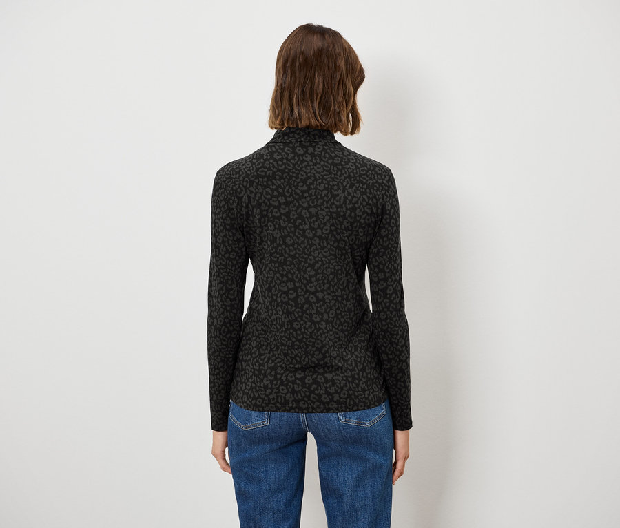Une femme, vue de dos, porte un pull noir à col roulé et un jean bleu.
