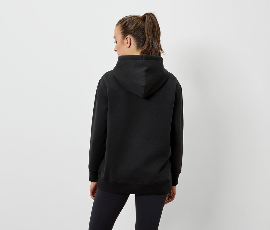 Une femme, vue de dos, porte un sweat à capuche noir et un legging noir.