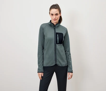 Une femme porte une veste en polaire verte avec un pantalon noir.