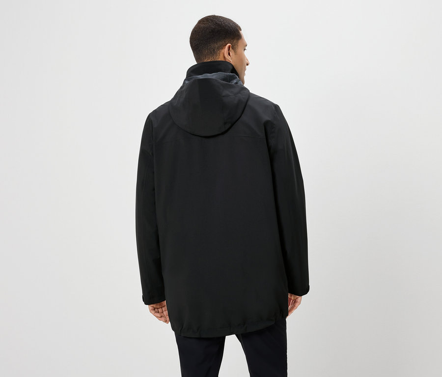 Un homme vu de dos porte une veste noire à capuche et un pantalon noir.