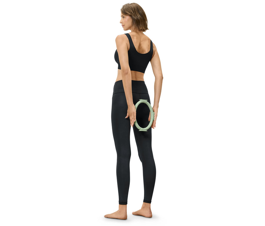 Femme en tenue de sport noire tenant un cercle vert derrière son dos.