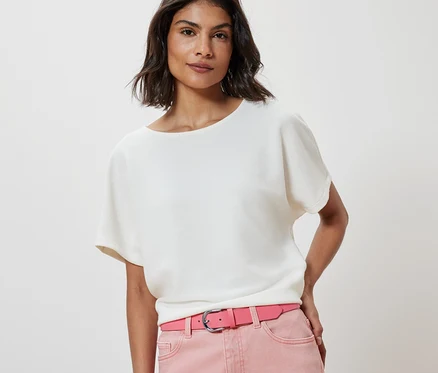 Une femme porte un chemisier blanc et une ceinture rose.