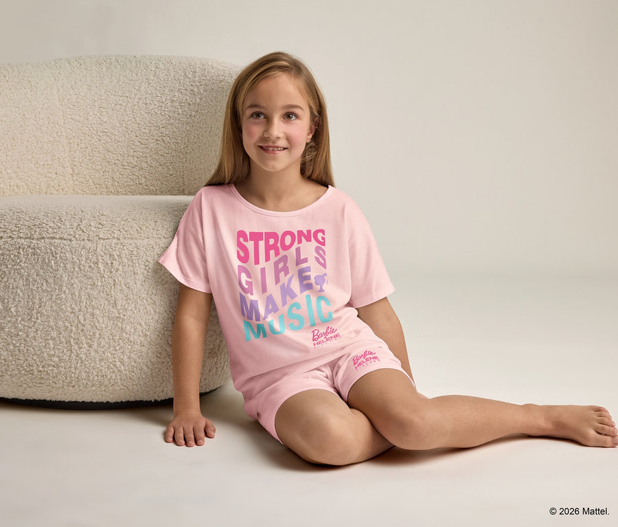Une fille est assise à côté d'un fauteuil et porte un pyjama rose avec l'inscription "Strong Girls Make Music".