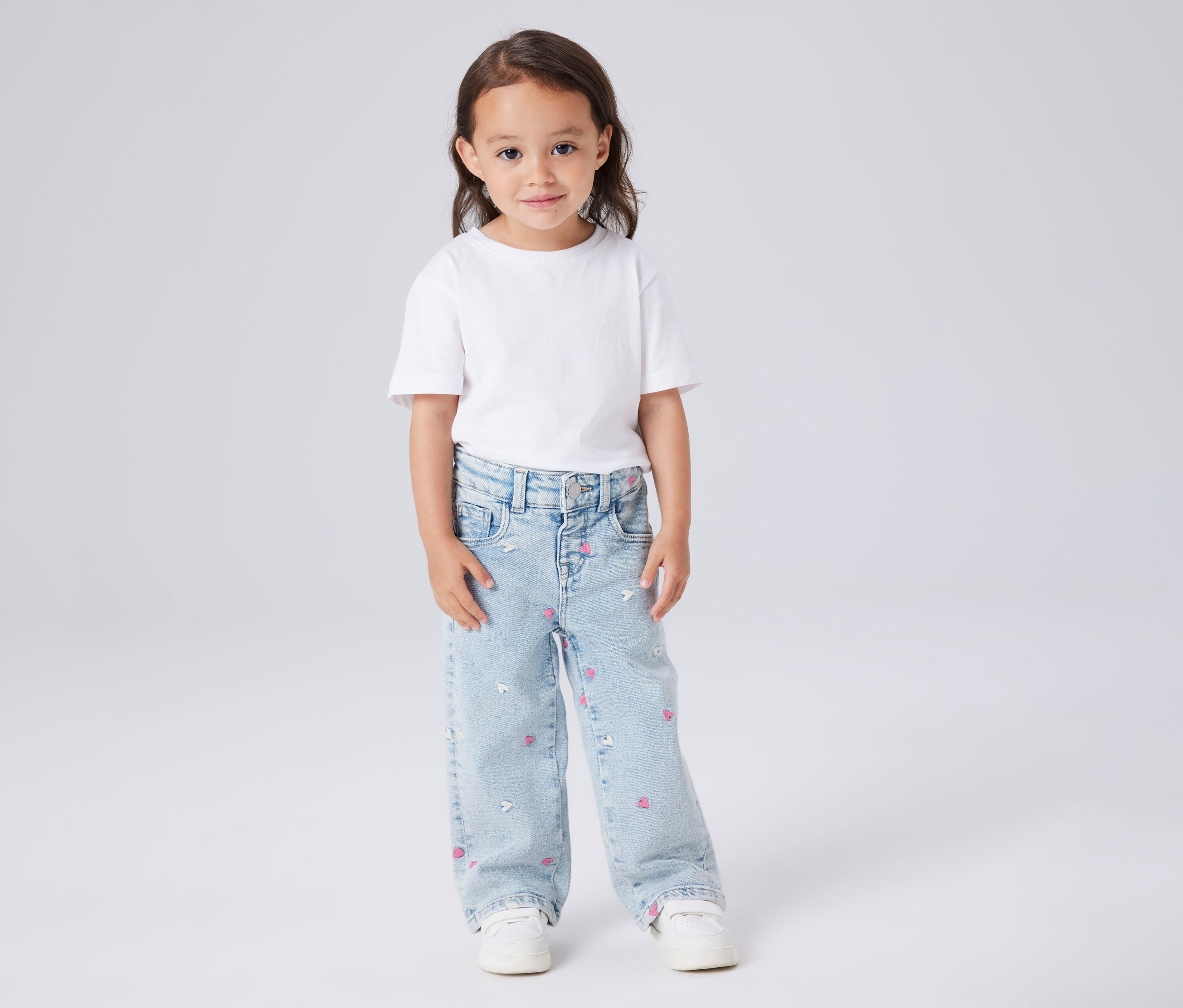 Une fille porte un t-shirt blanc et un jean à jambes larges pour enfant NAME IT avec des cœurs roses et des motifs de souris blanches.