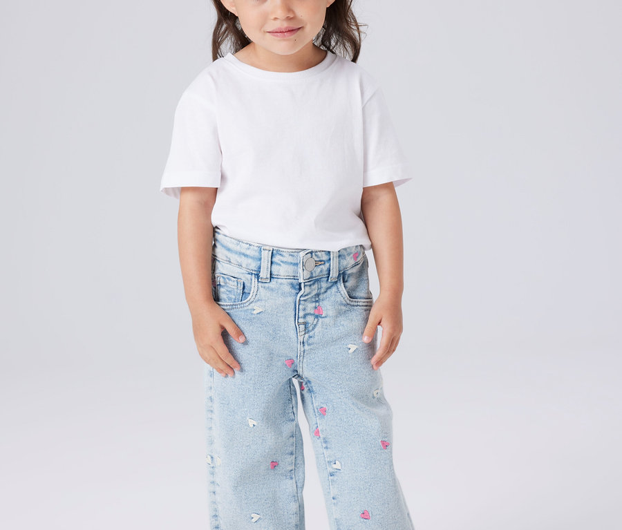 Fillette portant un t-shirt blanc et un jean bleu clair avec des motifs de cœurs et de souris.