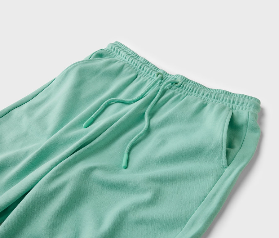 Gros plan d'un pantalon de jogging vert menthe avec cordon de serrage et poche sur fond blanc.