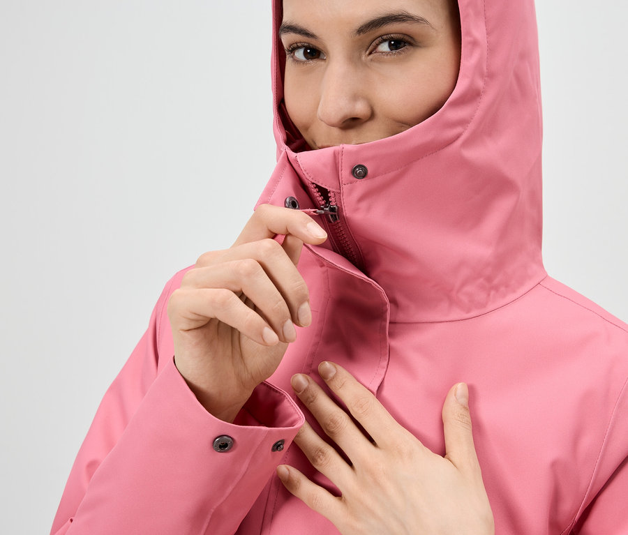 Femme fermant la fermeture éclair d'un imperméable rose à capuche.