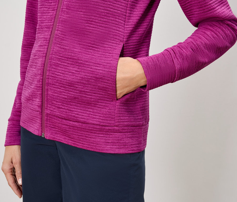 Gros plan d'une personne portant une veste zippée rose et un pantalon bleu marine, avec une main dans la poche de la veste.