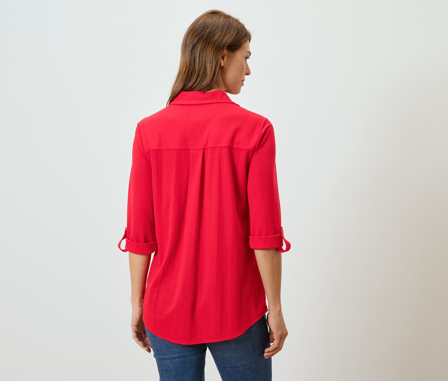 Vue arrière d'une femme aux longs cheveux bruns portant un chemisier rouge à manches longues et un jean.