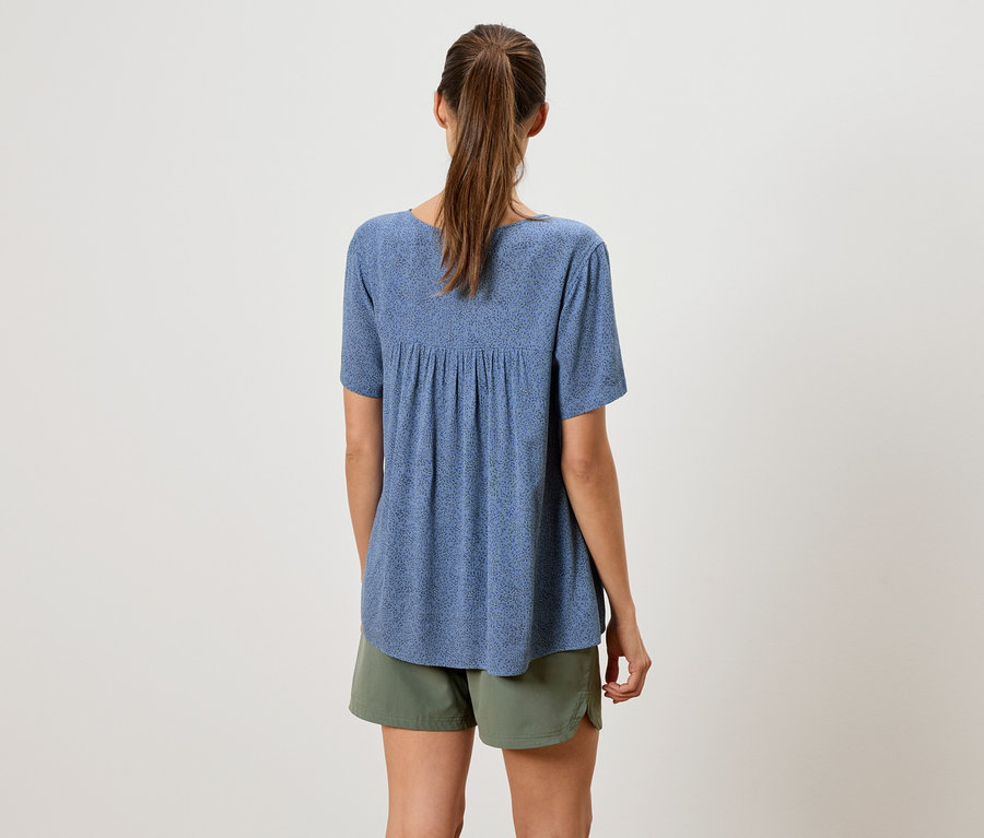 Vue arrière d'une femme avec une queue de cheval portant un chemisier bleu à manches courtes et un short vert olive.