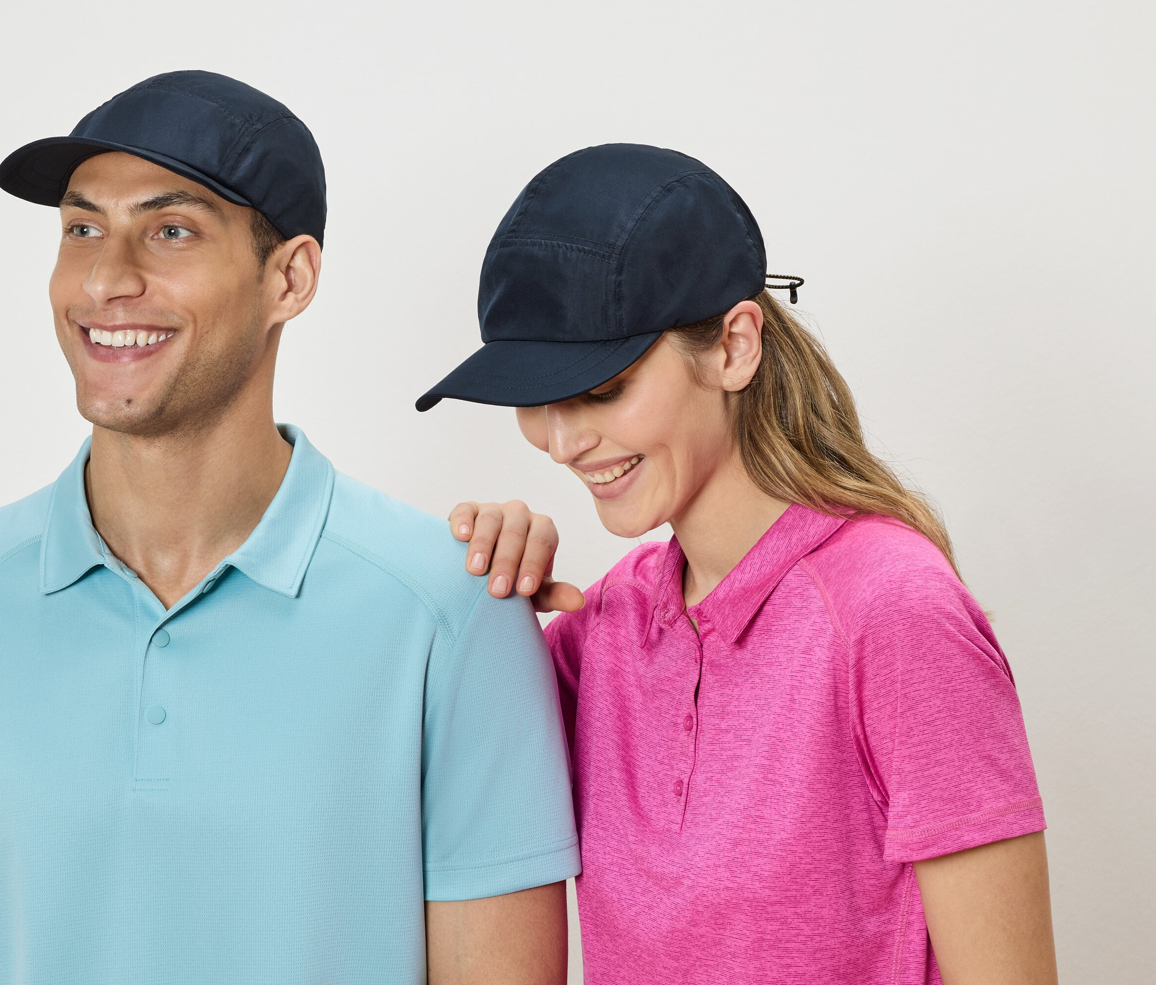 Un homme et une femme se tiennent côte à côte, portant des casquettes bleu marine et des polos bleus et roses.