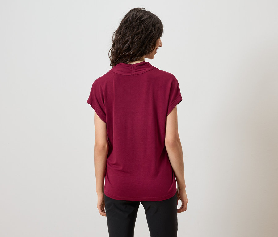 Vue arrière d'une femme aux cheveux ondulés et foncés, portant un haut bordeaux et un pantalon noir.