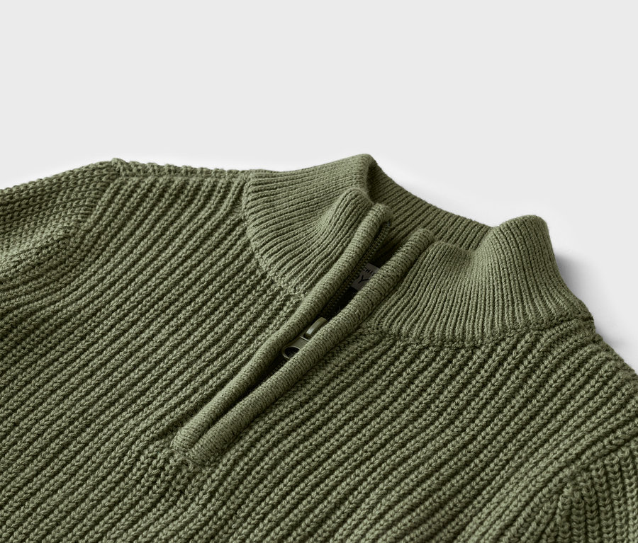 Gros plan d'un pull en tricot vert olive avec une courte fermeture éclair au niveau du col.