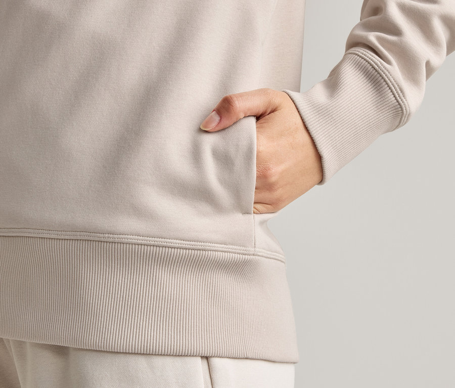 Gros plan d'une personne qui met sa main dans la poche d'une veste marron clair.