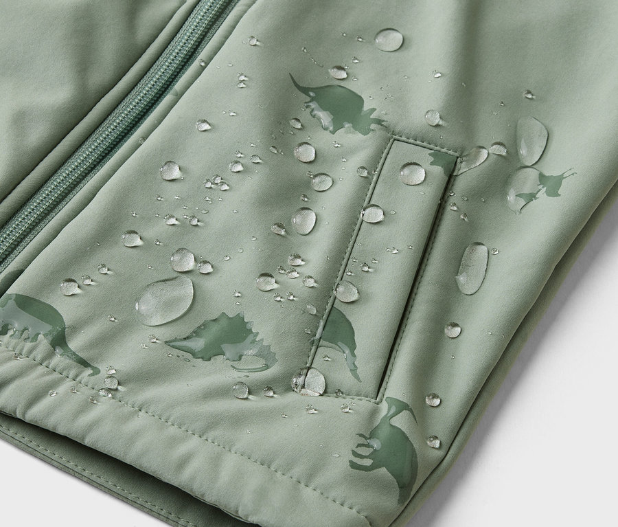Gros plan d'une veste vert clair avec fermeture éclair, poche et motif dinosaure, recouverte de gouttes d'eau.