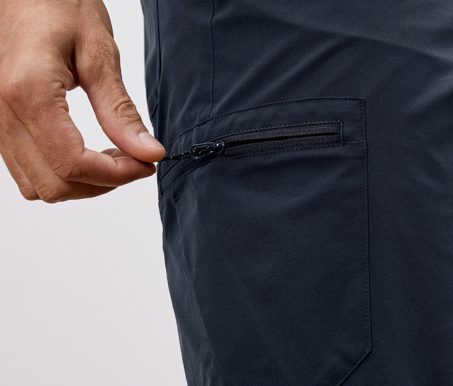 Gros plan d'une main fermant la fermeture éclair d'un pantalon bleu marine.