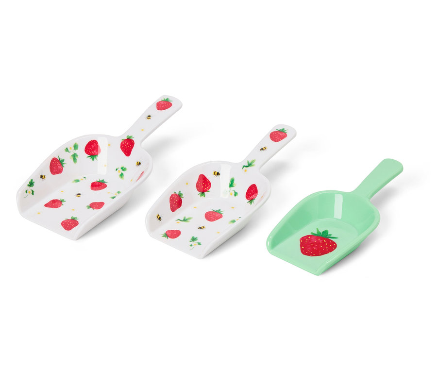 Trois pelles sont posées sur un fond blanc. Deux sont blanches avec un motif de fraises et une est verte avec un motif de fraises.