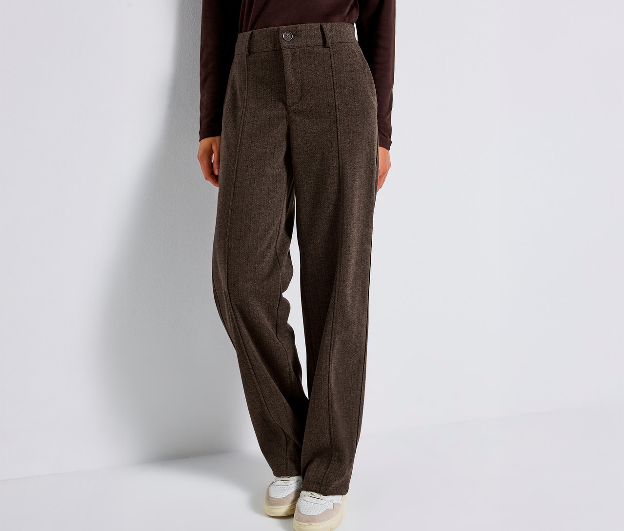 Une personne porte un pantalon marron Straight Leg Street One et des baskets sur un fond blanc.