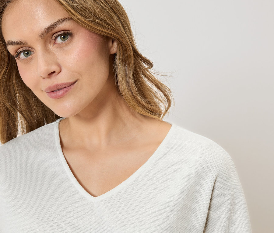 Portrait d'une femme blonde portant un pull blanc à col en V.