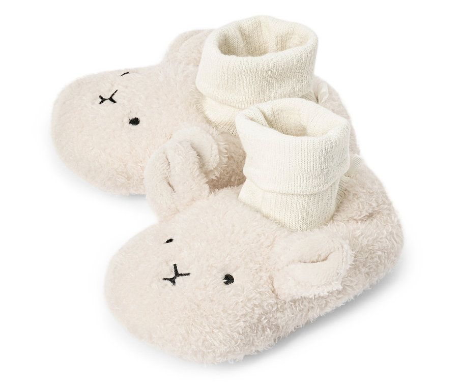 Gros plan sur une paire de chaussons pour bébé crème et duveteux avec un visage de lapin et des chaussettes blanches