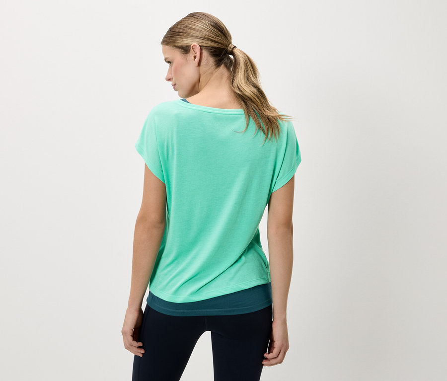 Vue arrière d'une femme blonde portant un t-shirt vert et un legging foncé.