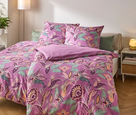 Linge de lit lilas à motifs floraux sur un lit fait.
