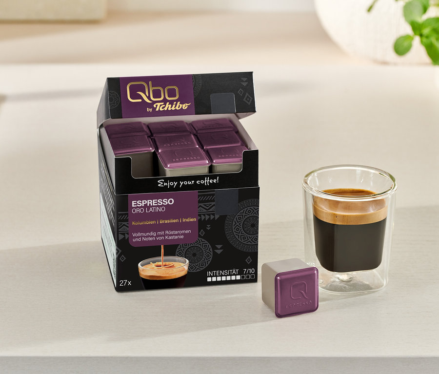 Une boîte ouverte de capsules Qbo Espresso ORO TOLIMA est à côté d'un verre d'espresso et d'une capsule individuelle.