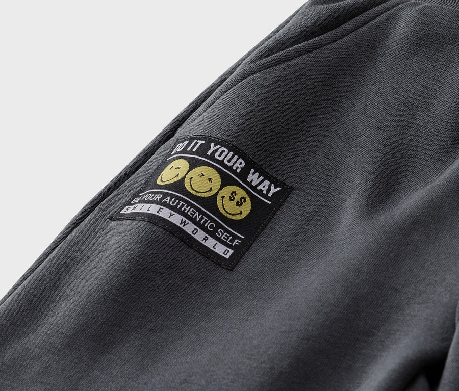 Gros plan d'un pantalon de jogging gris avec un patch noir avec des smileys jaunes et le texte "Do it your way".