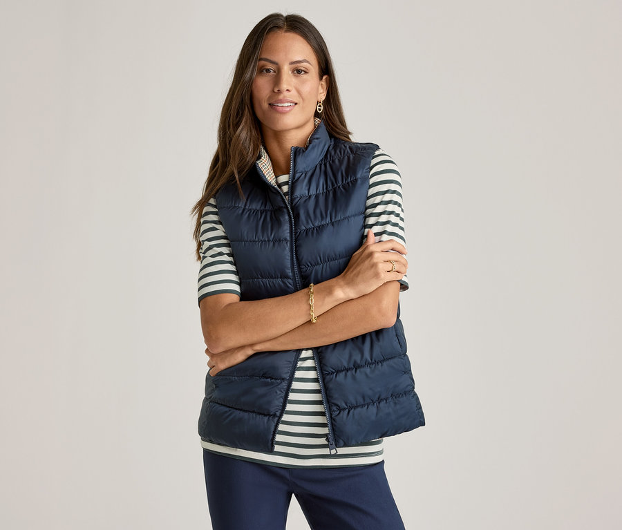 Une femme les bras croisés porte un gilet bleu marine sur un T-shirt demi-manches, vert à rayures.