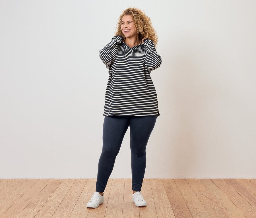 Femme aux cheveux bouclés portant un haut rayé, un legging et des baskets blanches.