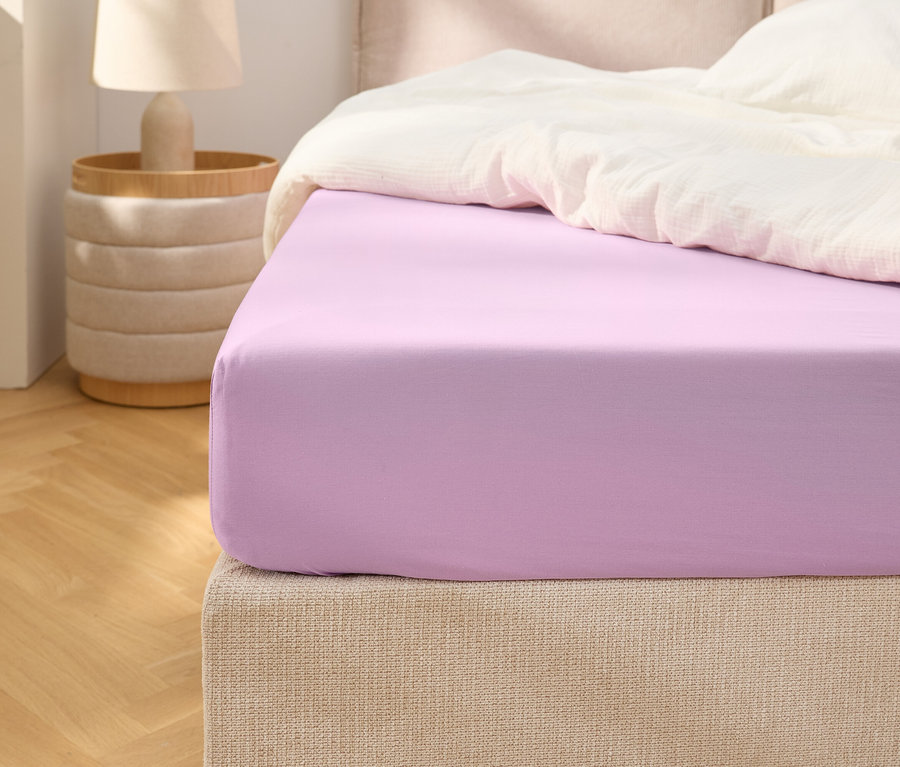 Gros plan d'un drap-housse violet sur un lit avec une couette blanche.