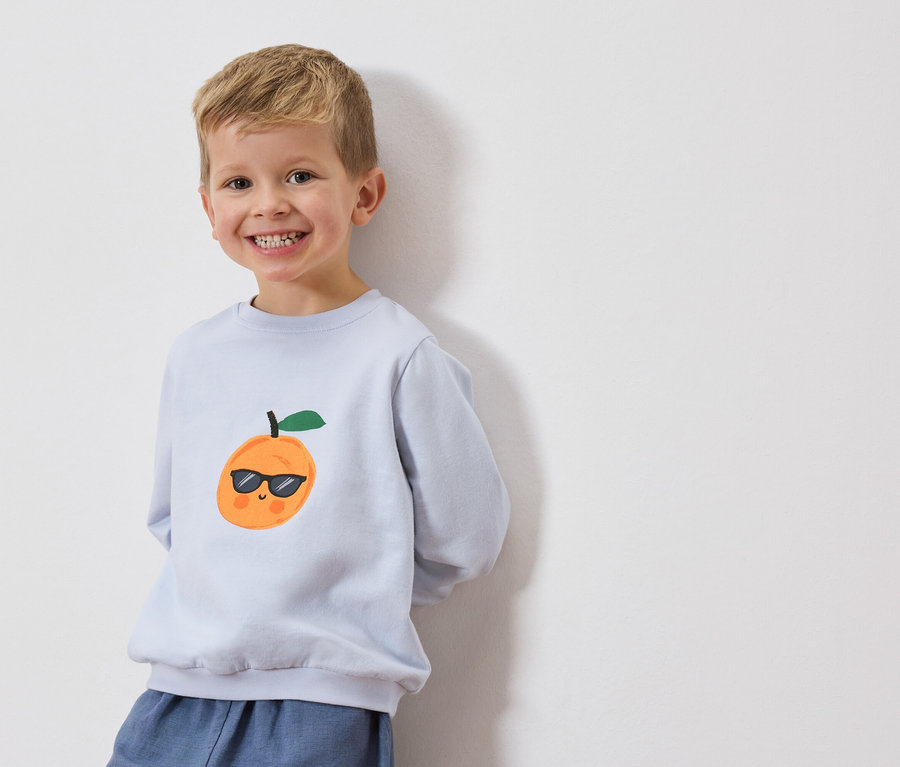 Un garçon souriant porte un sweat-shirt bleu clair avec une orange portant des lunettes de soleil.
