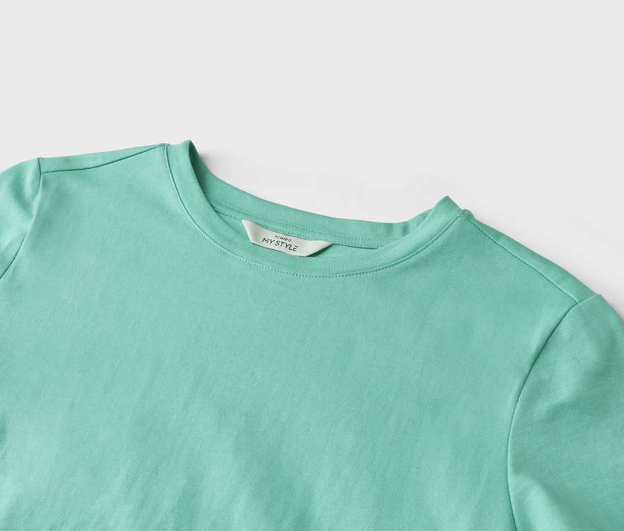 Gros plan d'un t-shirt turquoise clair avec une étiquette portant l'inscription "TCHIBO MY STYLE".