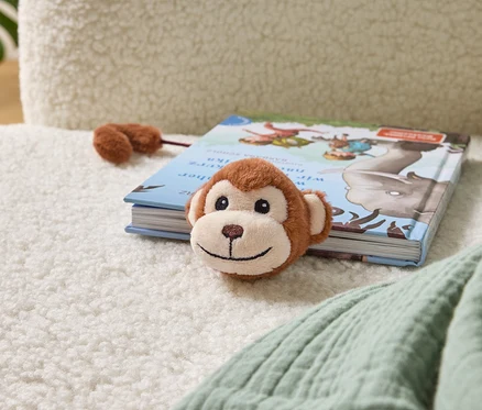 Un singe en peluche repose sur un livre pour enfants sur un fauteuil.