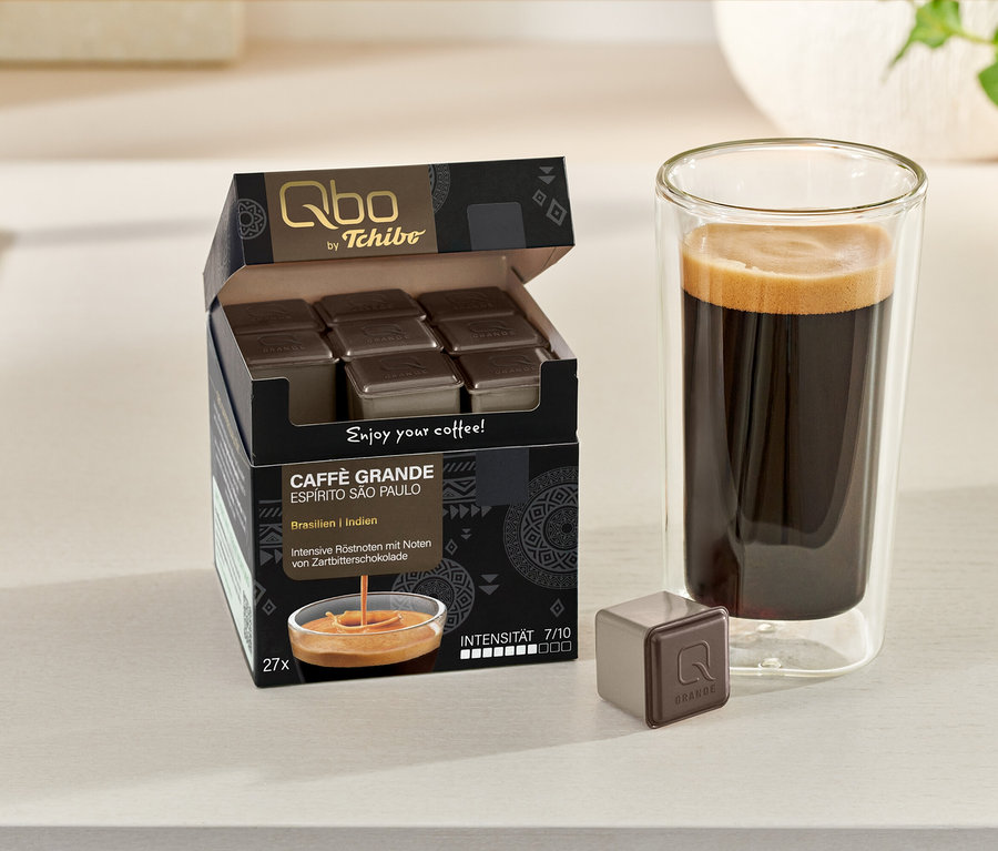 Boîte ouverte de capsules Qbo Caffè Grande ESPÍRITO SÃO PAULO et un verre de café. Une capsule est posée à côté.