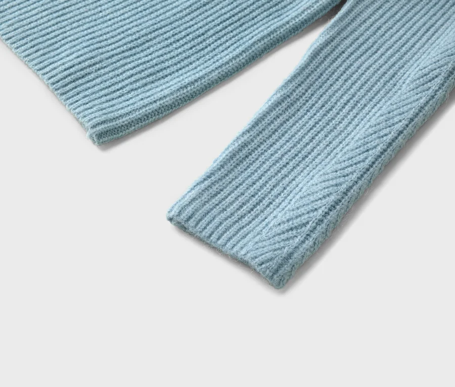 Gros plan d'un pull en tricot côtelé bleu clair avec une manche et un ourlet sur fond blanc.