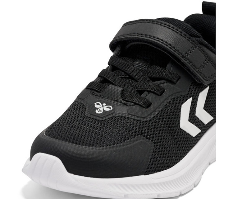 Baskets hummel® « Actus Tr Bearther Jr » noires avec semelle blanche, fermeture velcro et lacets. Chevrons Hummel blancs sur le côté et logo abeille sur la languette.
