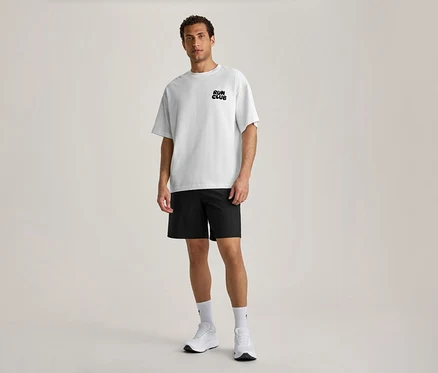 Un homme se tient de face, portant un T-shirt de sport blanc avec l'inscription noire « RUN CLUB » sur la poitrine, un short noir, des chaussettes blanches et des chaussures de sport blanches.