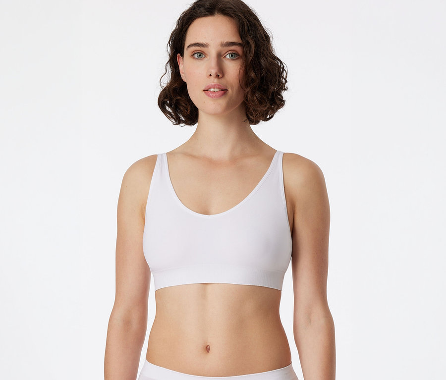 Femme aux cheveux courts et bouclés porte une brassière douce SCHIESSER blanche avec coussinets et regarde l'objectif.
