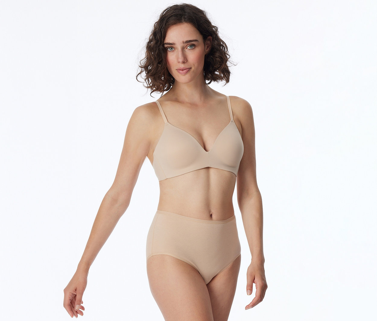 Femme aux cheveux courts et bouclés, portant un soutien-gorge et une culotte taille haute beiges, regardant l'appareil photo.