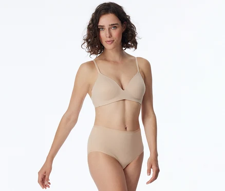 Femme aux cheveux courts et bouclés, portant un soutien-gorge et une culotte taille haute beiges, regardant l'appareil photo.