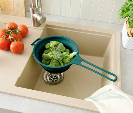 Brocoli dans une passoire bleue au-dessus de l'évier, tomates à droite, pot de basilic en arrière-plan.