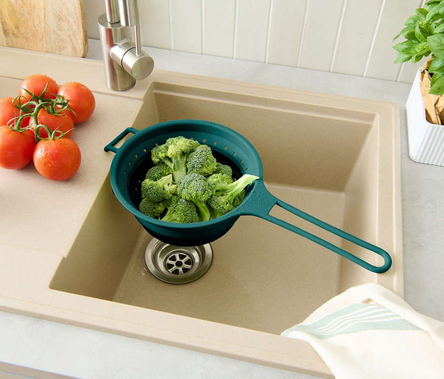 Brocoli dans une passoire bleue au-dessus de l'évier, tomates à droite, pot de basilic en arrière-plan.