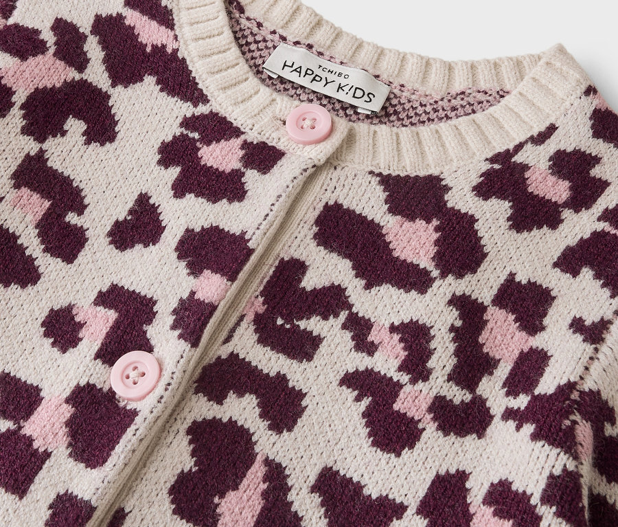 Gros plan d'un cardigan crème avec un imprimé léopard rose foncé et rose clair. Il a des boutons rose clair et une étiquette "Happy Kids" sur le col.