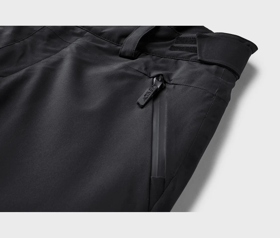 Gros plan d'un pantalon noir montrant une poche zippée avec une tirette "ACTIVE", un passant de ceinture et une sangle réglable.