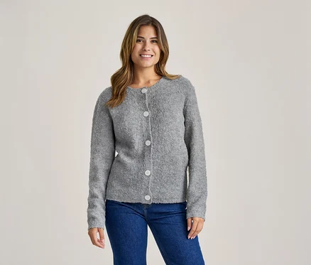 Femme souriante portant un cardigan gris texturé boutonné et un jean bleu.