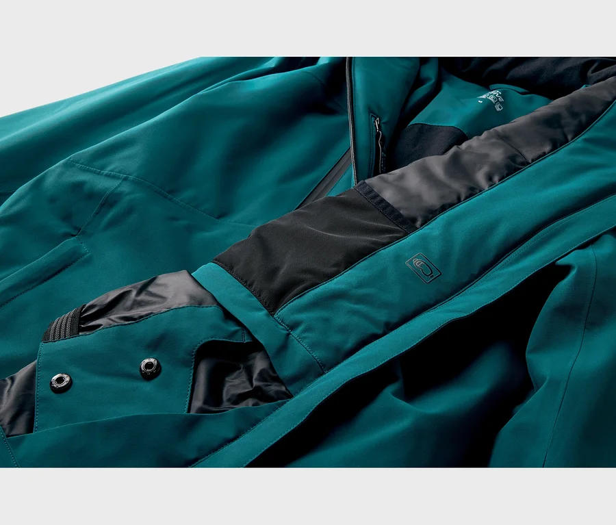 Gros plan d'une veste technique sarcelle avec doublure noire, fermeture éclair visible, deux boutons-pression et un logo de lunettes en relief sur le col.