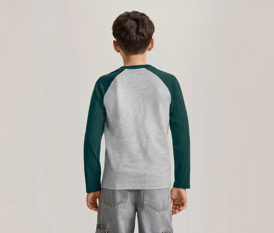 Un jeune garçon vu de dos, portant un t-shirt raglan à manches longues gris et vert foncé et un short gris.
