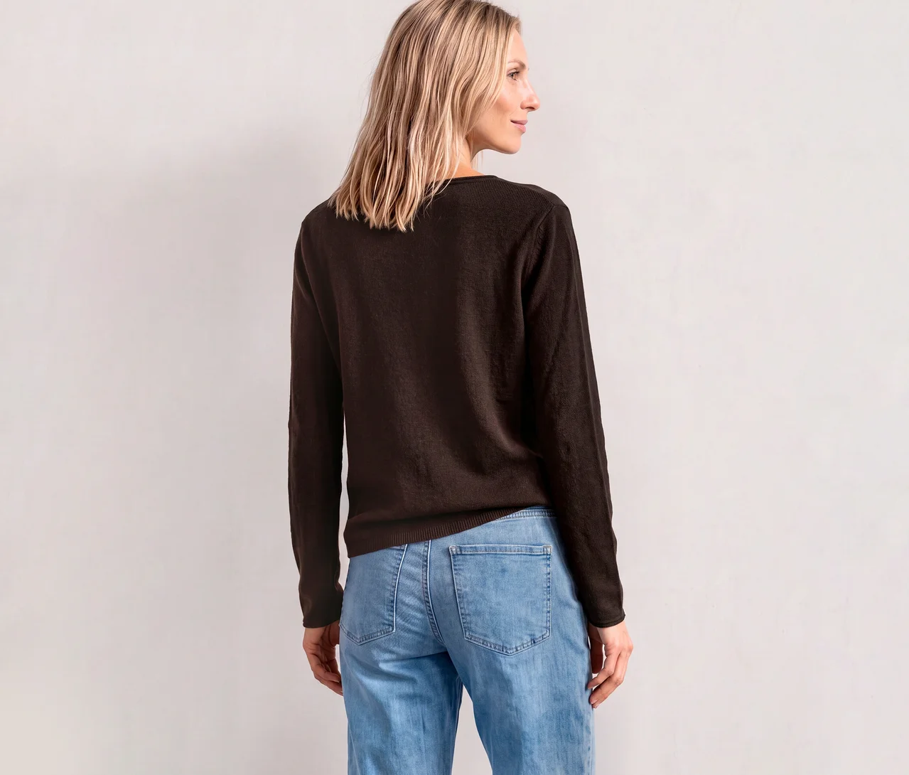Femme de dos portant un pull en maille Street One marron et un jean bleu clair, regardant par-dessus son épaule droite.