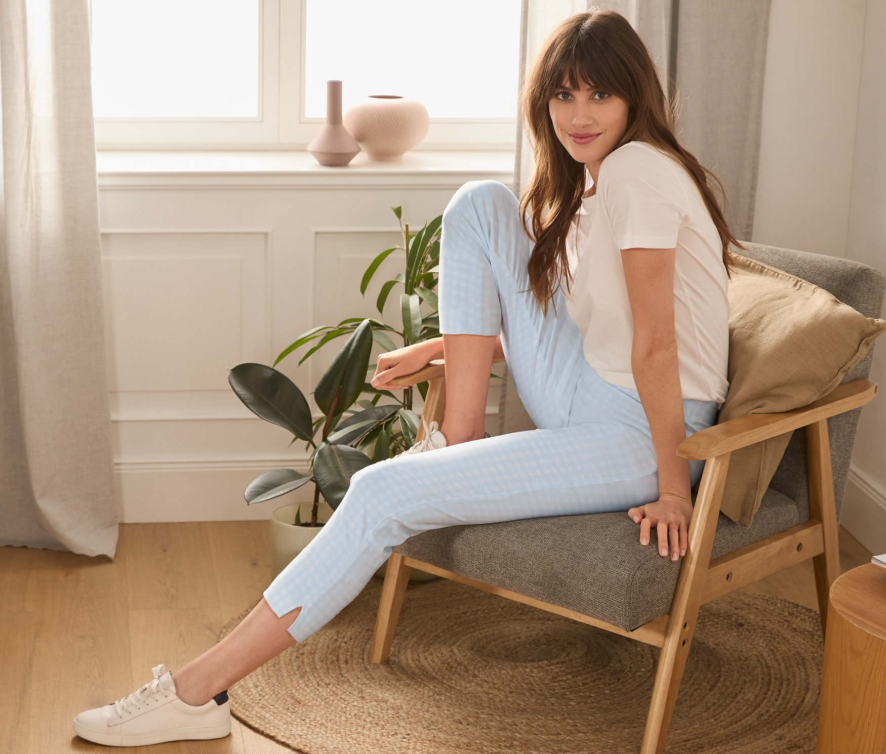 Une femme est assise dans un fauteuil et porte un pantalon stretch 7/8 bleu clair et blanc.